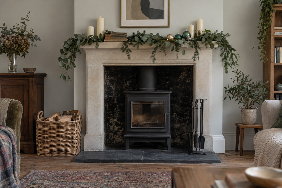 A fireplace mantel dressed for winter with a eucalyptus and fir garland, candles and glass baubles.