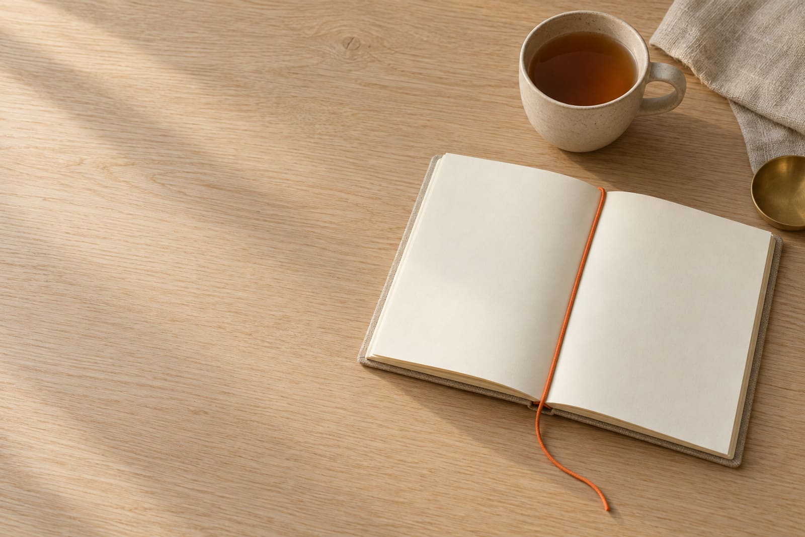 An open notebook with blank pages and an orange paper cord as its bookmark, beside a stoneware cup of tea.